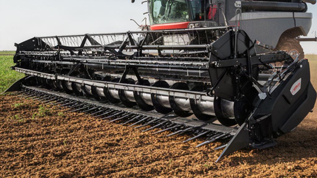 Plataforma de corte agrícola apoyada sobre suelo de tierra junto a una cosechadora